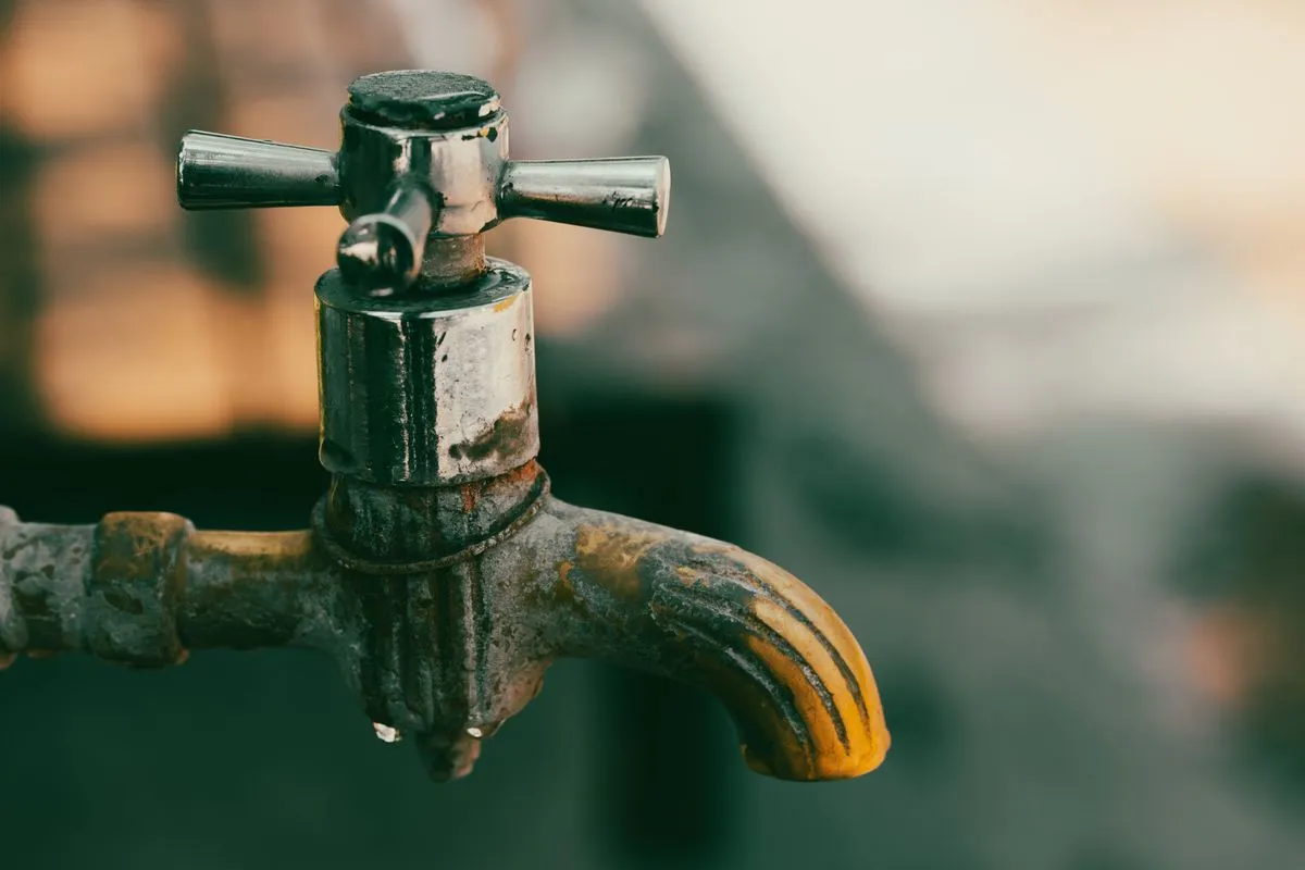 Robinet ancien en métal couvert de dépôts, une goutte d'eau au bec
