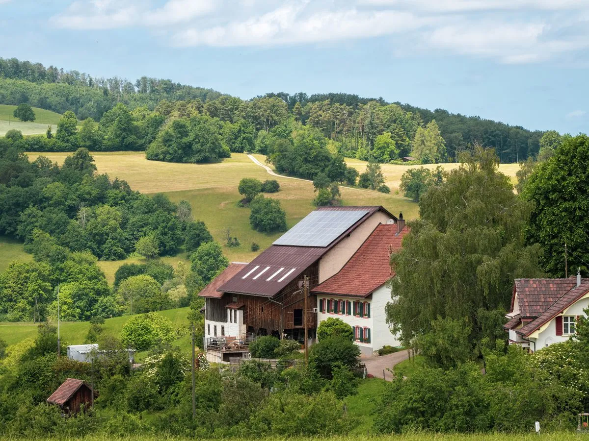 Ferme à la campagne avec panneaux solaires sur le toit, entourée de prés et de forêts